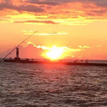 A fishing rod stands in the water, silhouetted against a vibrant sunset sky.