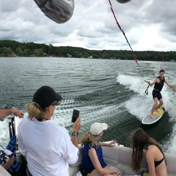 A group of people on a boat watches a wakeboarder performing tricks on the water