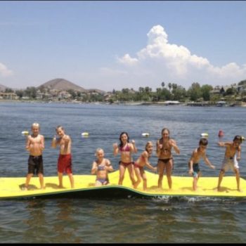 A group of kids enjoying leisure time on a floating raft in calm water under a clear sky.