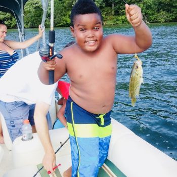 A young boy proudly holds a fish while sitting on a boat with his family