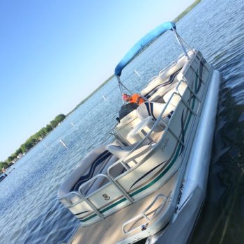 A pontoon boat featuring a blue canopy, floating gently on calm waters under a clear sky.