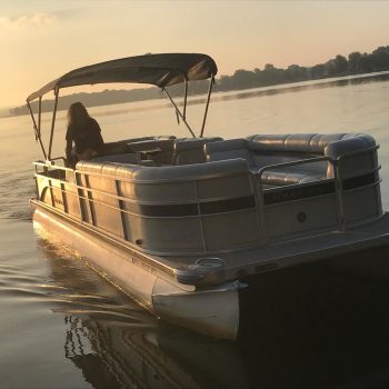 A person navigates a pontoon boat across calm waters under a clear sky