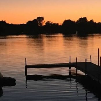 A serene dock extends into the water, illuminated by the warm hues of a sunset sky.