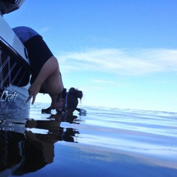 A person crouching to observe a boat, showcasing curiosity and engagement with the watercraft.