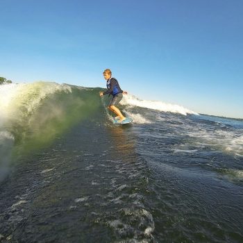 A kid skillfully rides a wave on a boat, showcasing his balance and control amidst the ocean's dynamic movement.