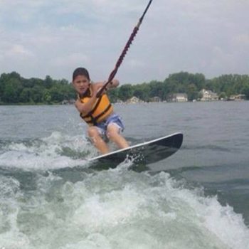 A young boy skillfully wakeboards on a serene lake